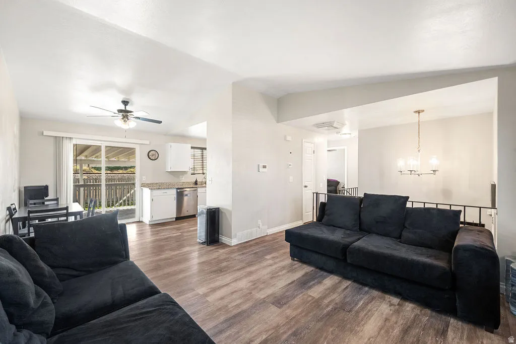 Living room featuring dark wood-type flooring, hanging lights, lofted ceiling, and a ceiling fan