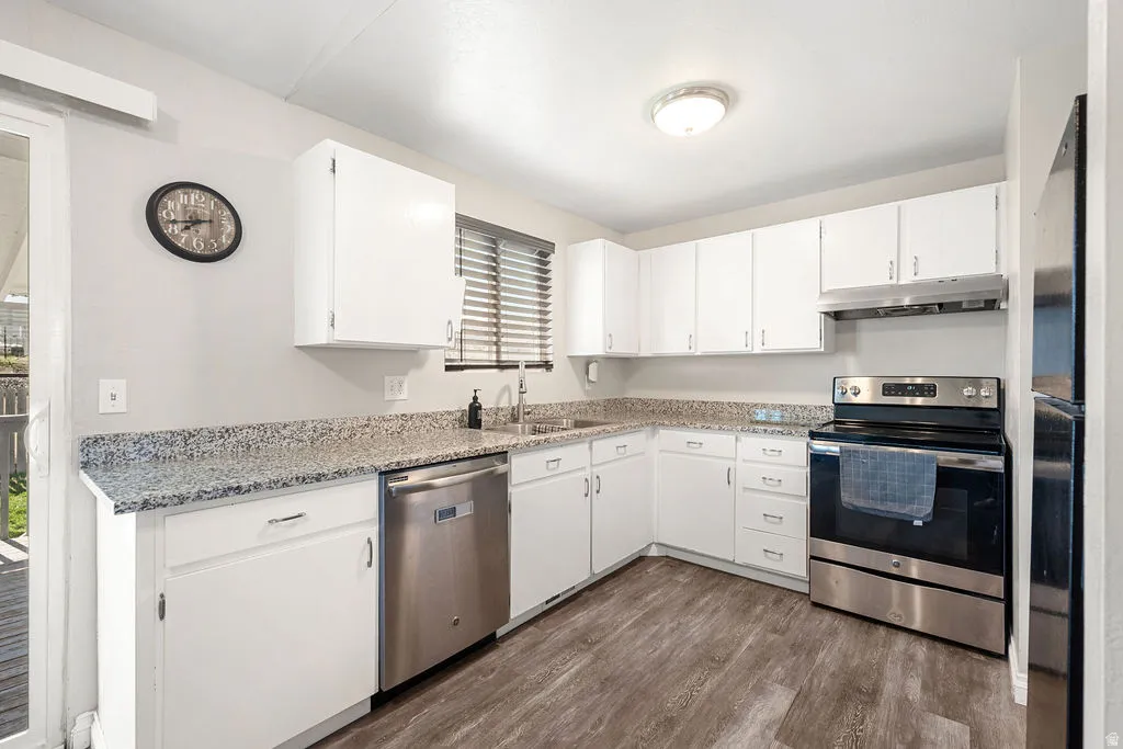 Kitchen featuring stainless steel appliances, white cabinets, light stone counters, and dark wood finished floors