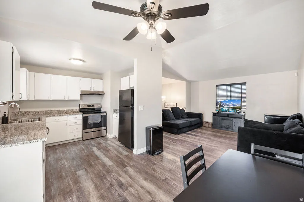 Kitchen with open floor plan, electric stove, white cabinetry, freestanding refrigerator, and vaulted ceiling