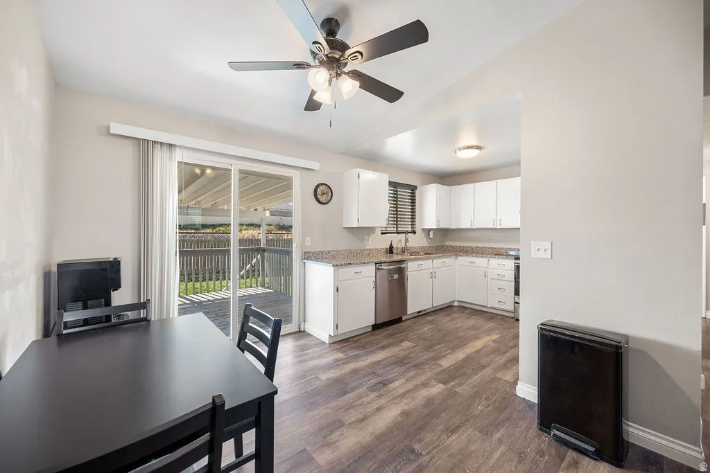 Kitchen with white cabinetry, ceiling fan, stainless steel dishwasher, dark wood-type flooring, and lofted ceiling