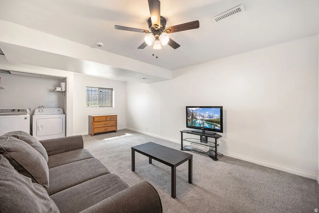 Living area with carpet floors, a ceiling fan, and independent washer and dryer