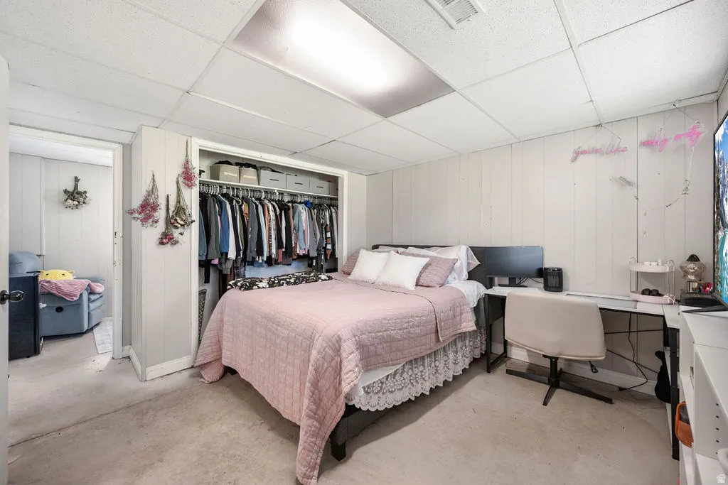 Bedroom with a drop ceiling, a desk, wood walls, concrete floors, and a closet