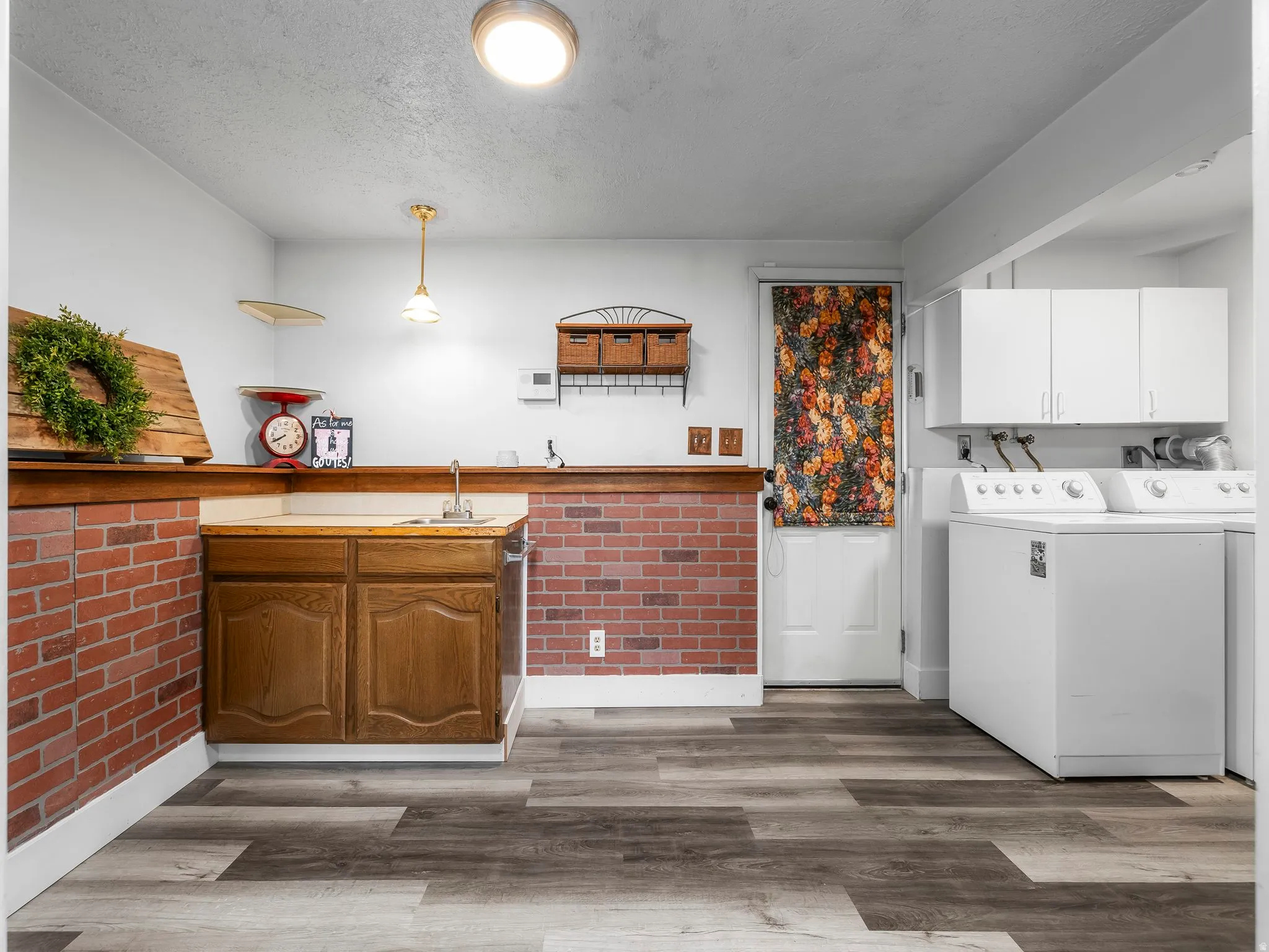 Laundry area featuring cabinet space, dark wood-type flooring, washer and dryer, a textured ceiling, and bar with sink