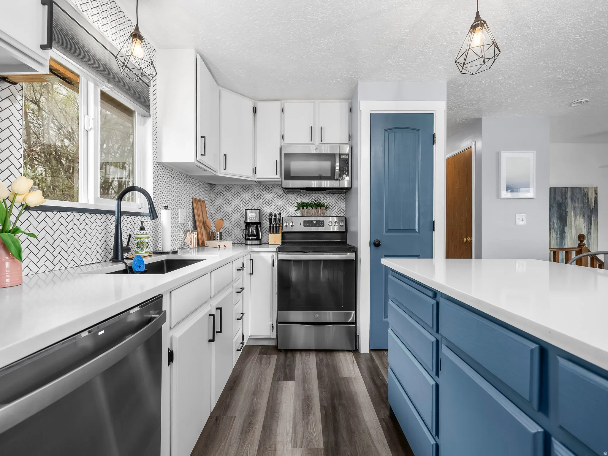 Dual tone kitchen with two tone color scheme, stainless steel appliances, pendant lighting, dark wood-style floors, and light stone countertops