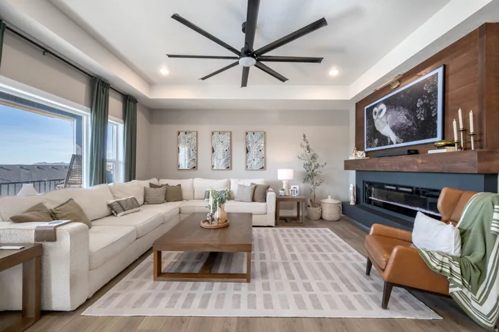 Living room featuring a ceiling fan, a tray ceiling, wood finished floors, a glass covered fireplace, and recessed lighting