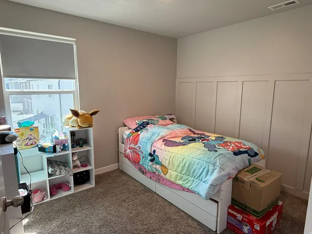 Bedroom featuring a decorative wall, carpet floors, and wainscoting