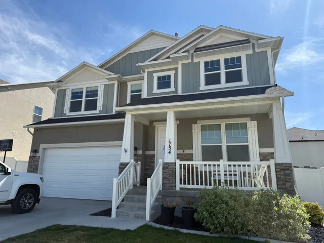 Craftsman-style house featuring stone siding, a garage, covered porch, board and batten siding, and driveway