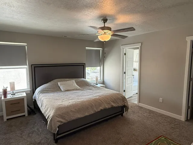 Bedroom with a textured ceiling, carpet flooring, and a ceiling fan
