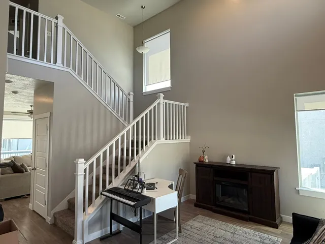 Stairs featuring wood finished floors, ceiling fan, a high ceiling, and a glass covered fireplace