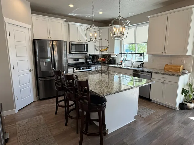 Kitchen with light stone countertops, stainless steel appliances, a kitchen breakfast bar, and white cabinets