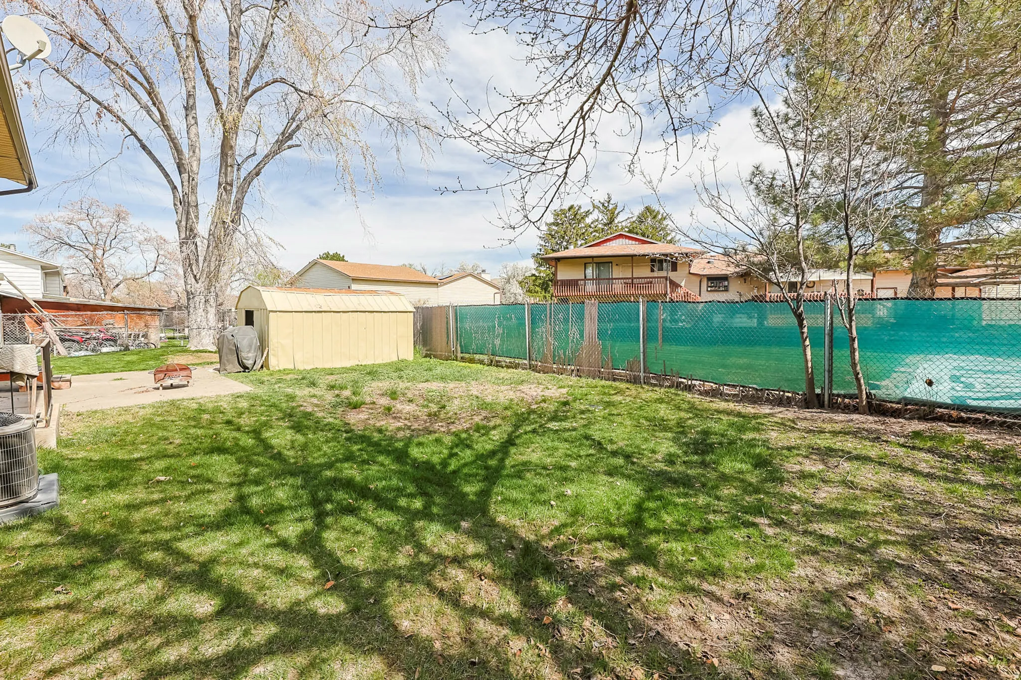 Expansive lawn with a chain-link fence, mature trees, and a concrete patio