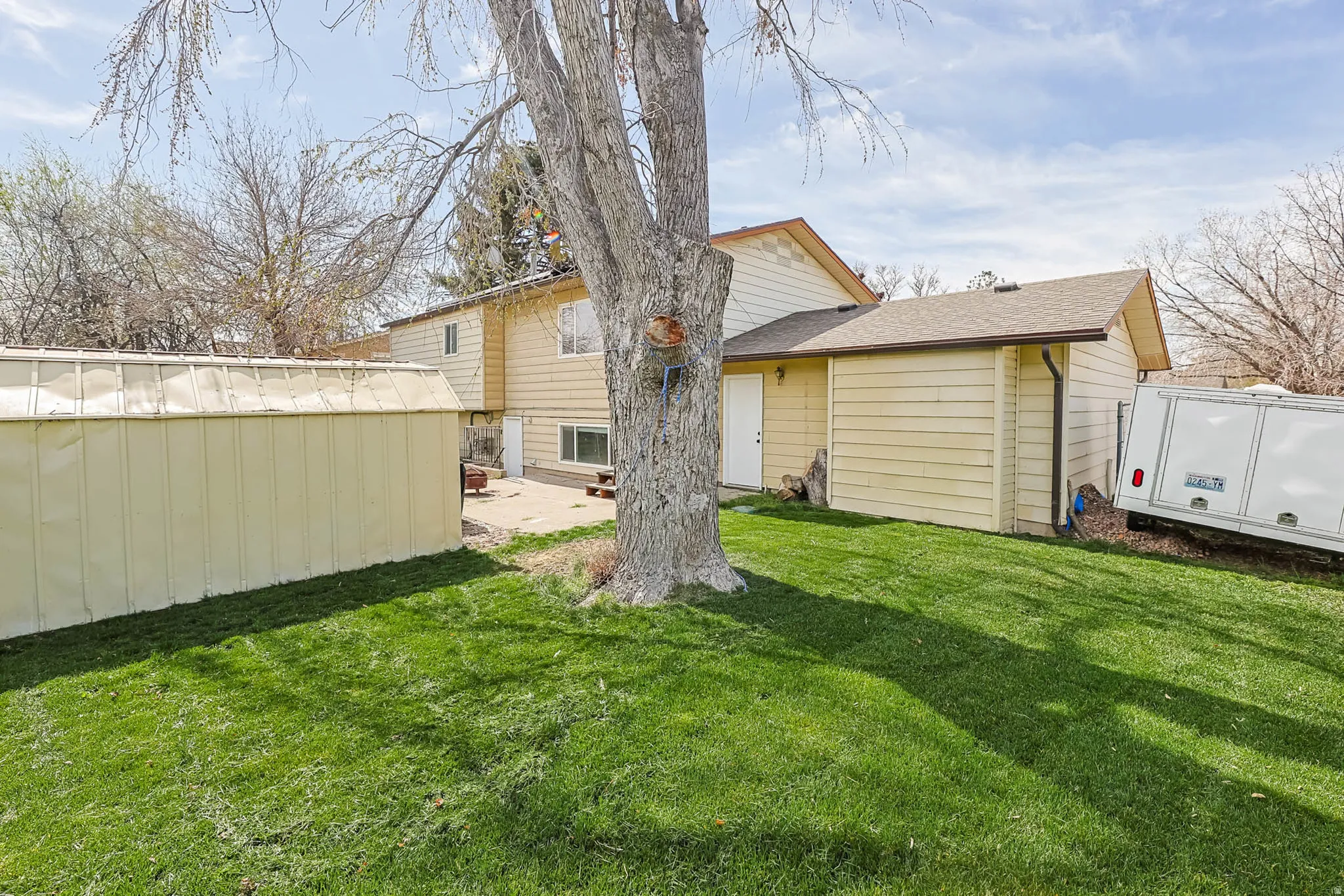 Expansive rear yard featuring green grass, a mature tree, and a building with horizontal siding