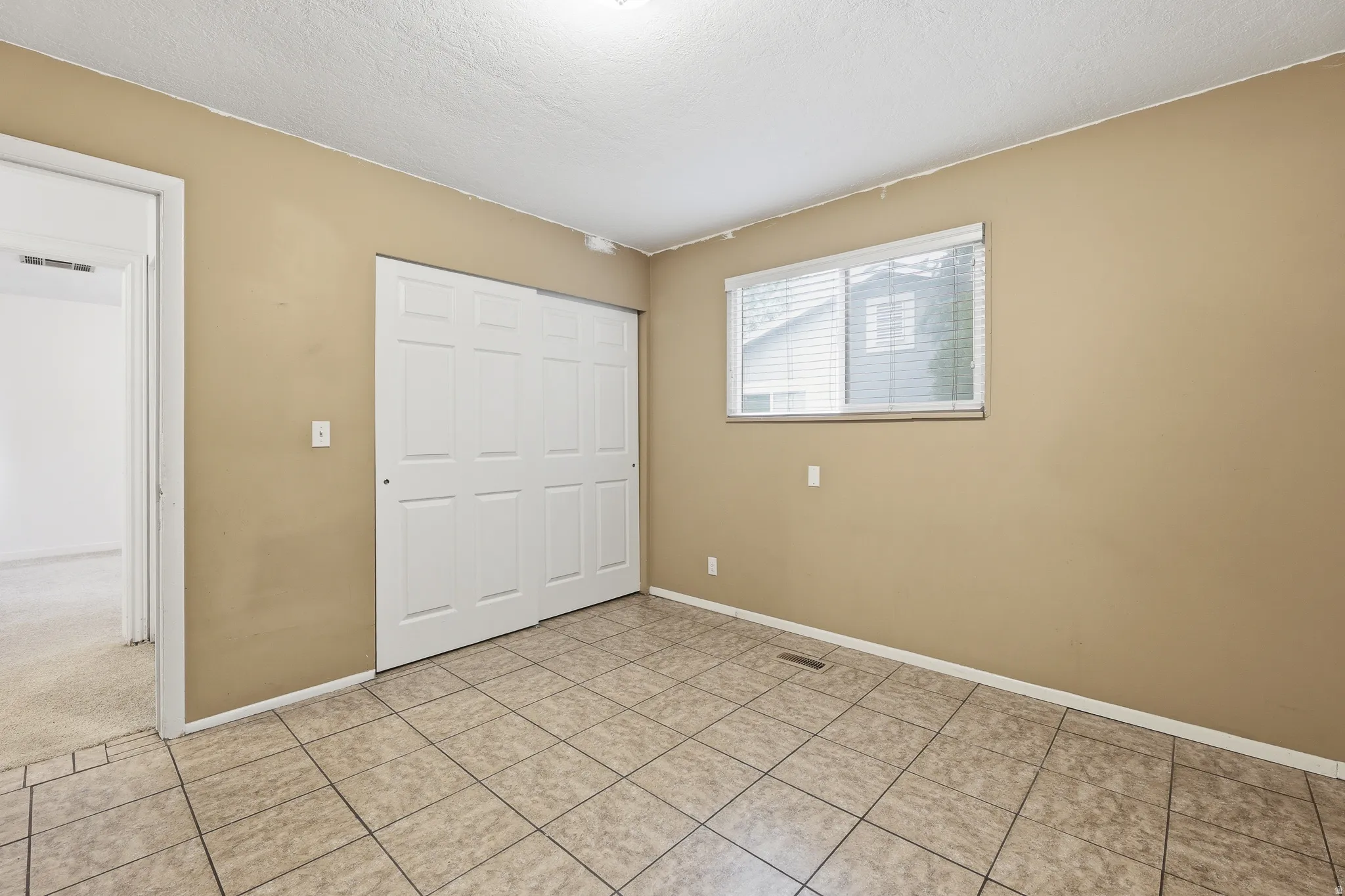 Spacious room featuring tile flooring, a window with blinds, and a closet with bifold doors
