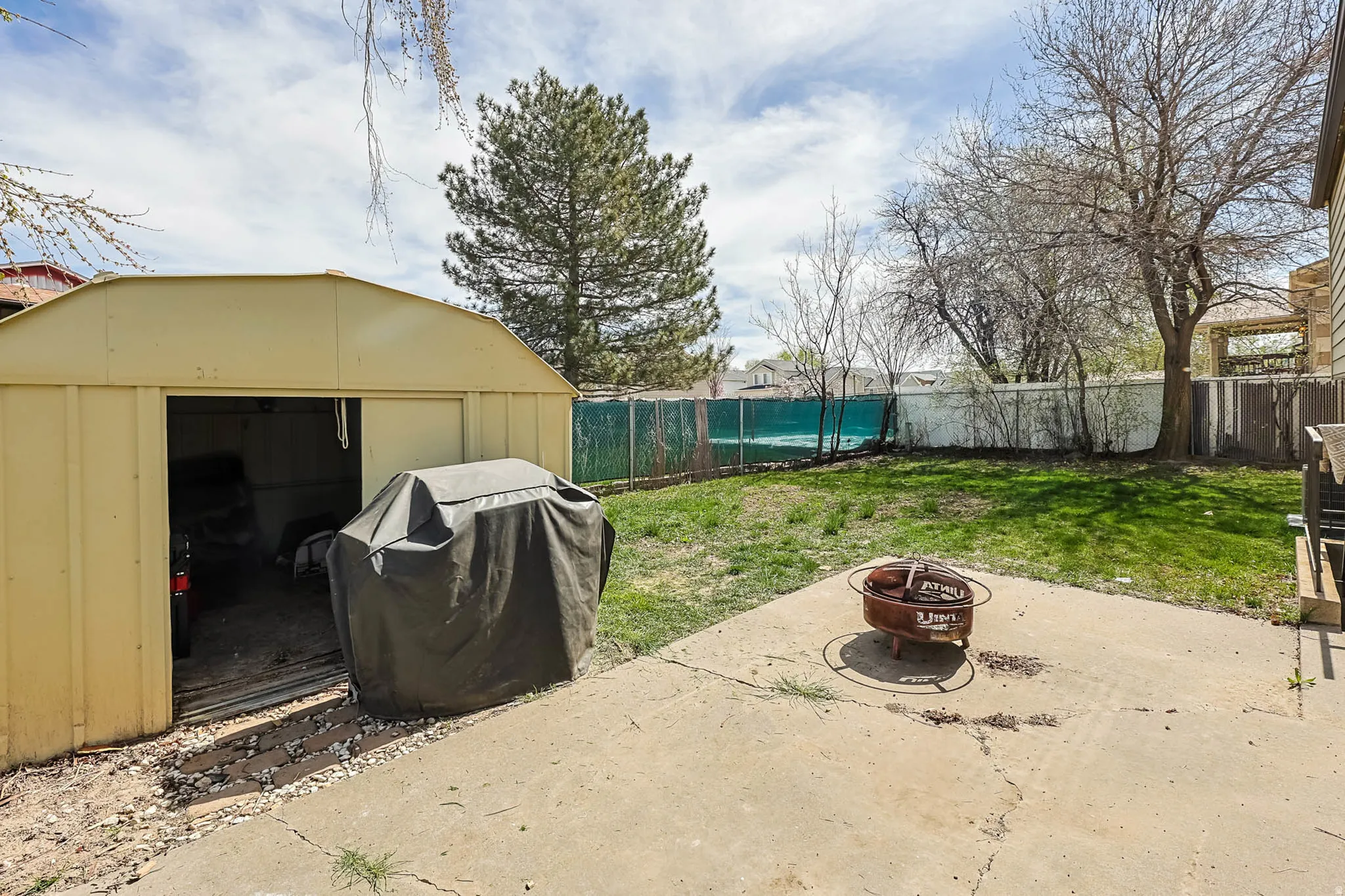Expansive backyard featuring a concrete patio, a freestanding storage shed, and a fenced perimeter