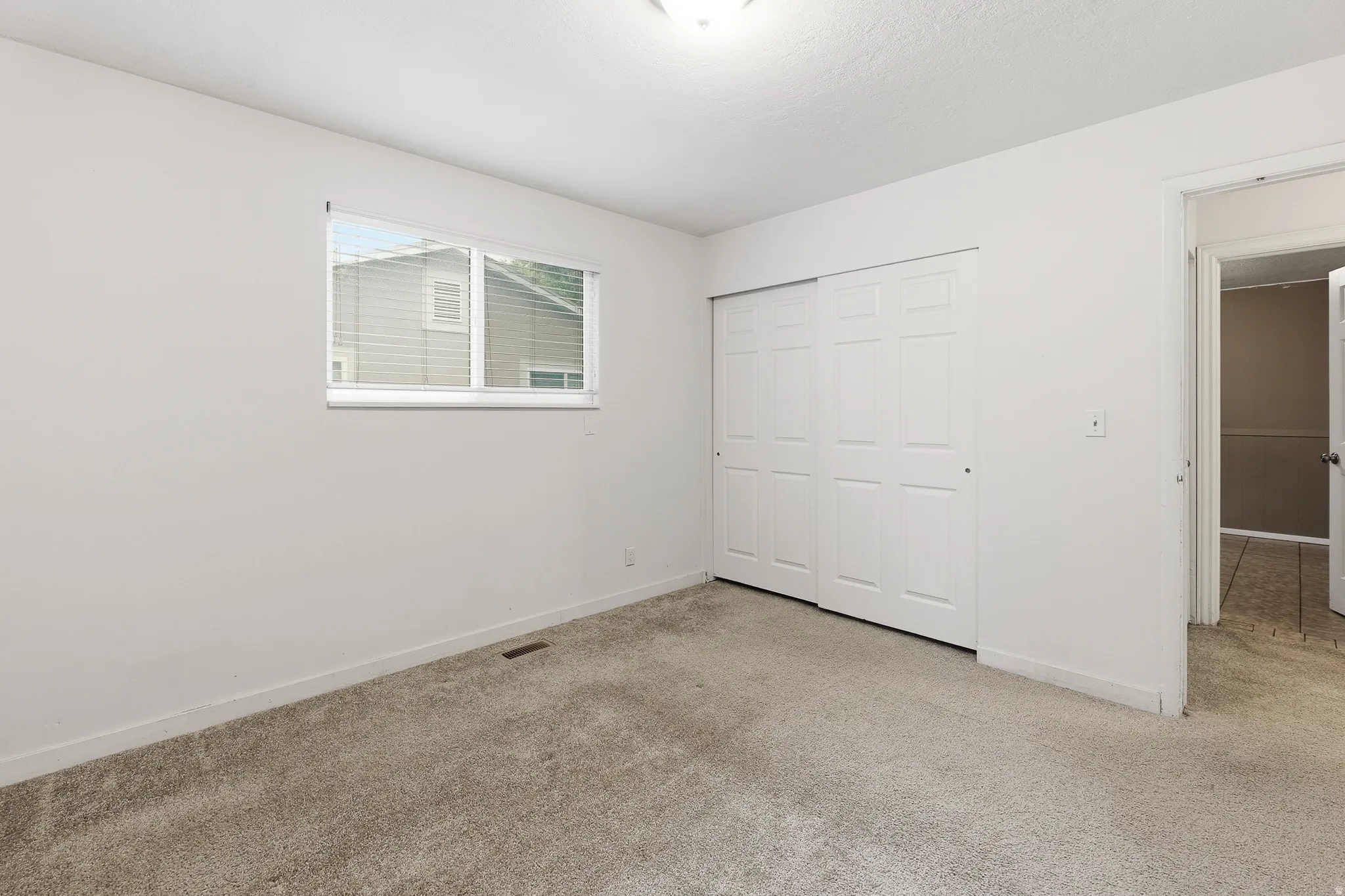 Carpeted interior space featuring light-colored walls and a window with blinds