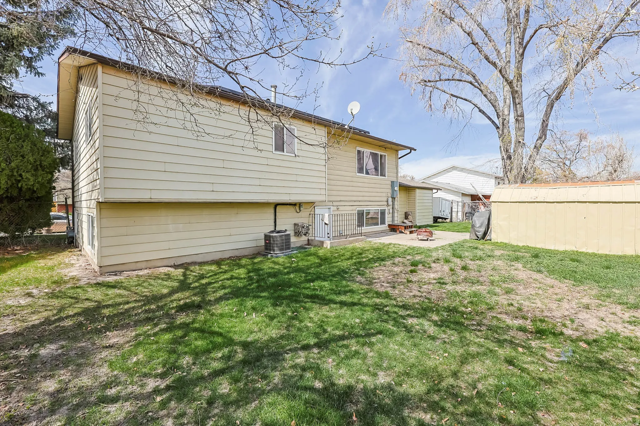 Spacious rear yard featuring a large patio, lush green lawn, and a storage shed