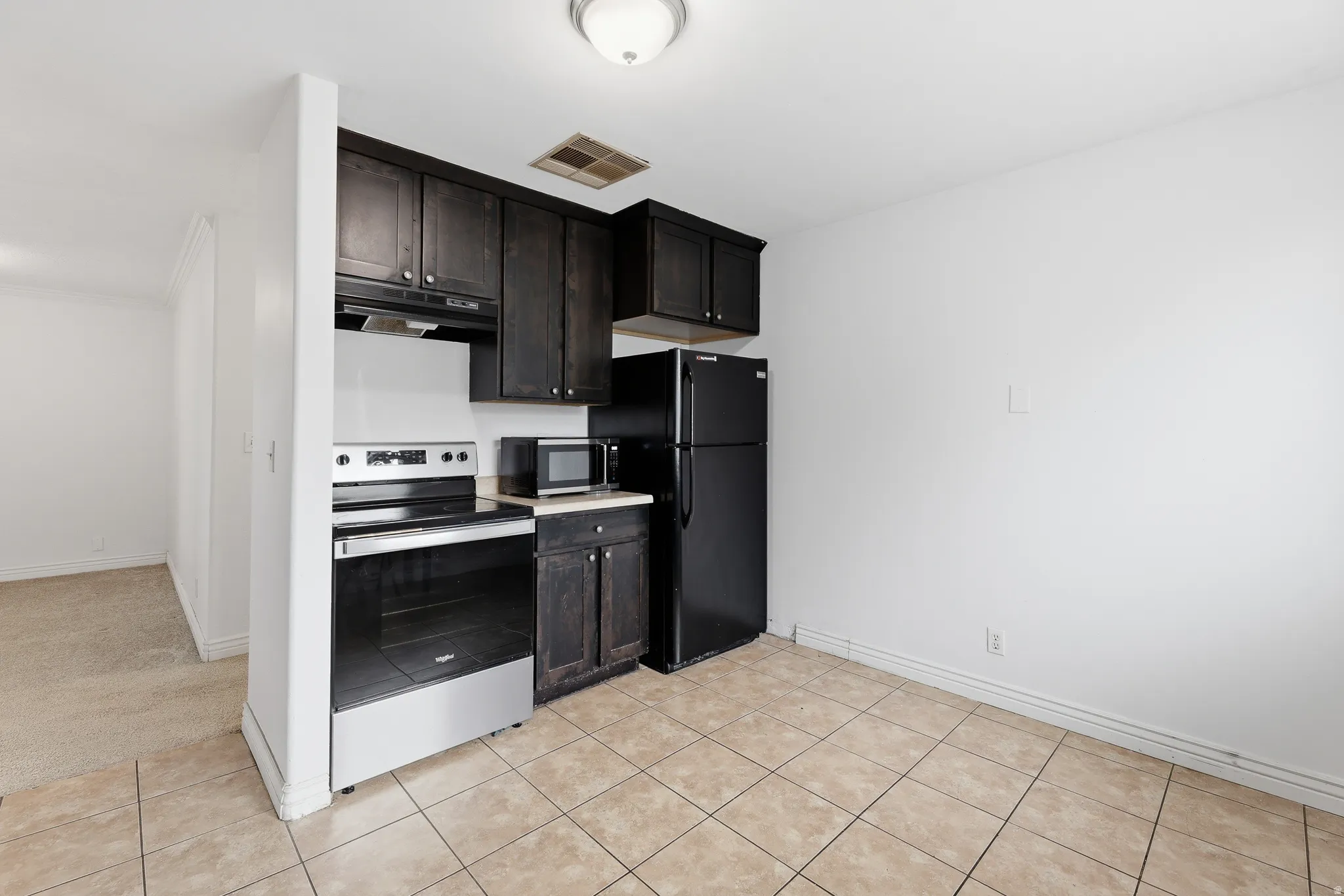 Kitchenette featuring dark wood-finish cabinetry, stainless steel range, and black refrigerator