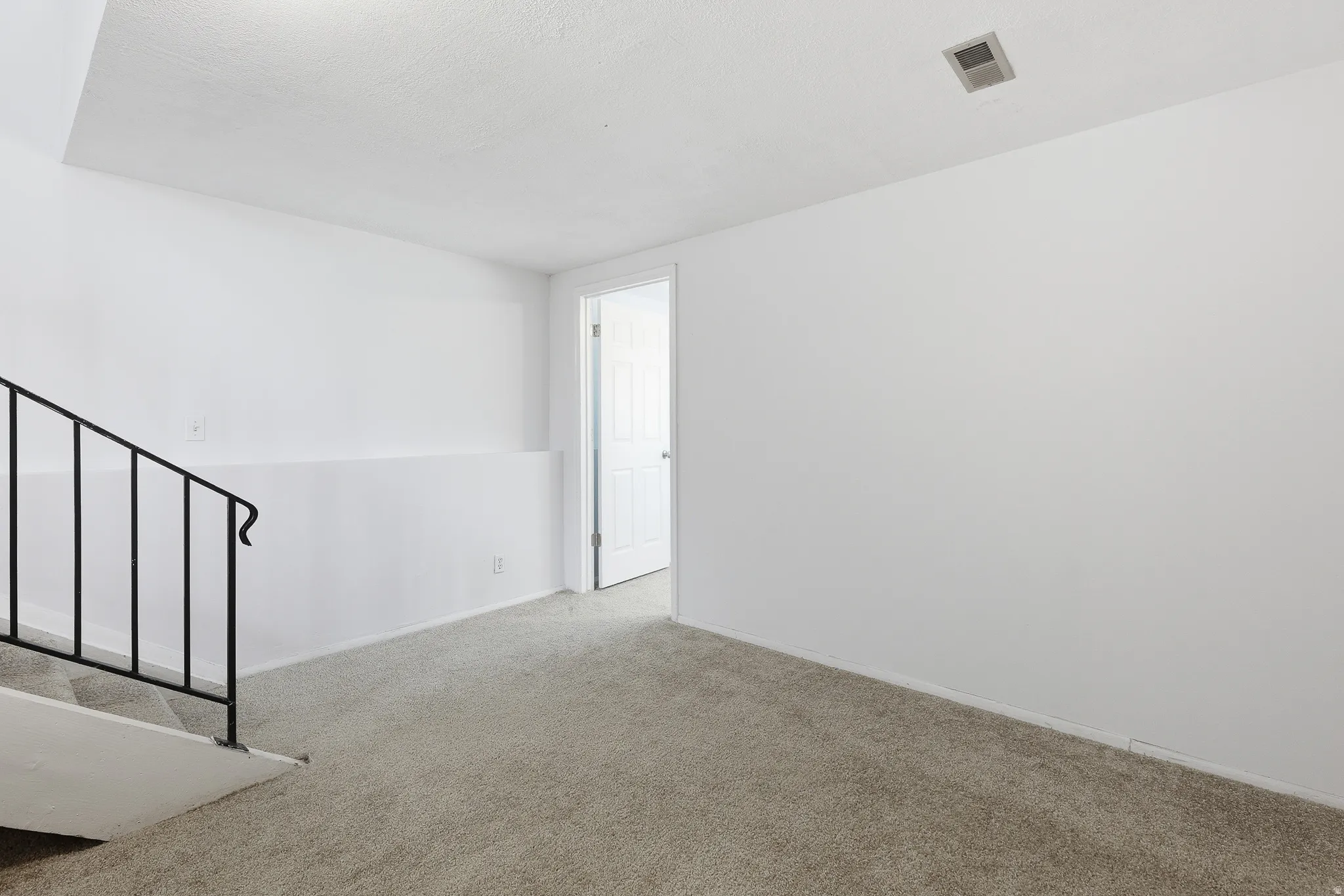 Carpeted room featuring a staircase with black metal railing, white painted walls, and a white paneled door