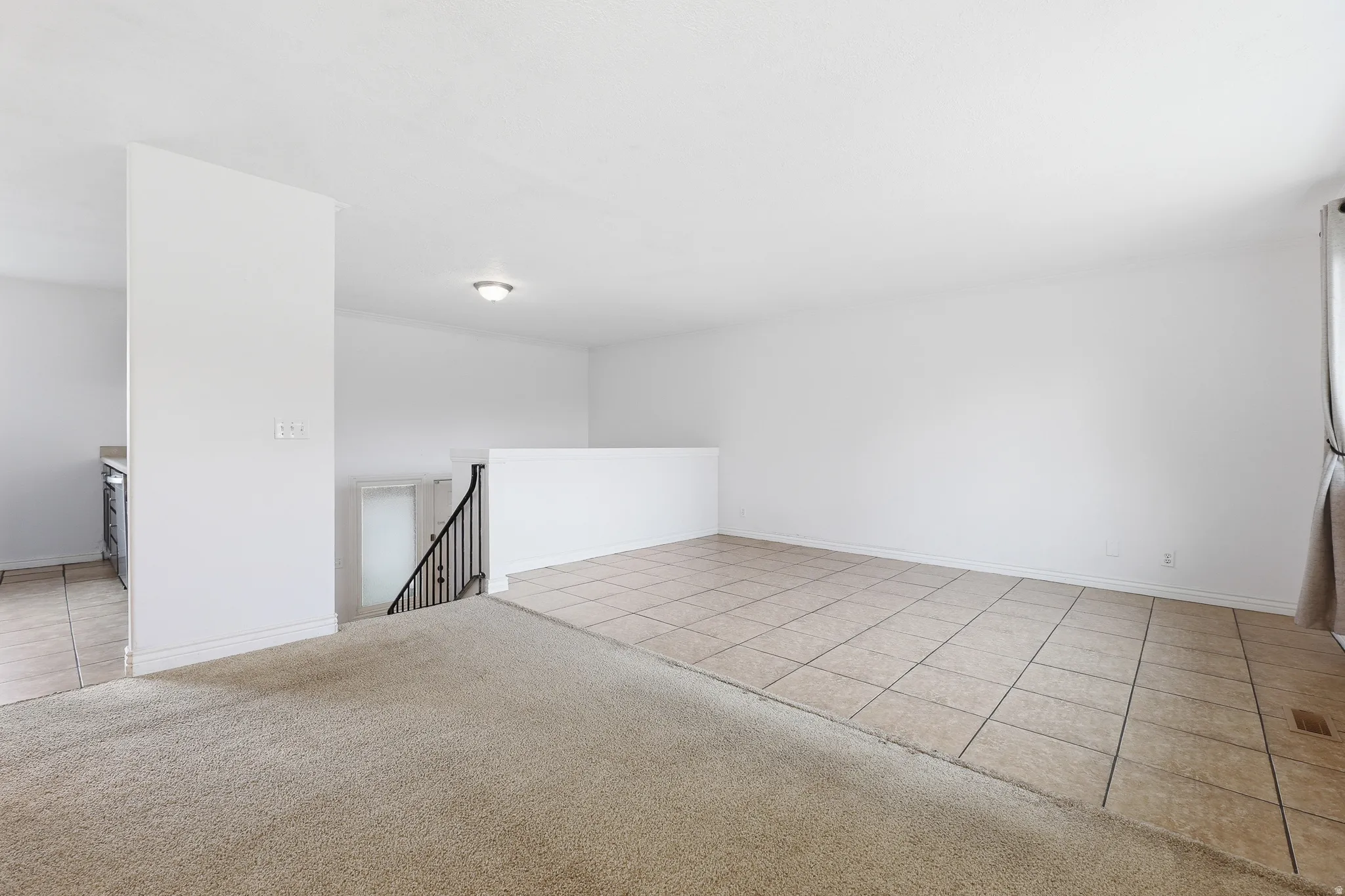 Spacious room featuring a combination of light-colored carpeting and large square floor tiles