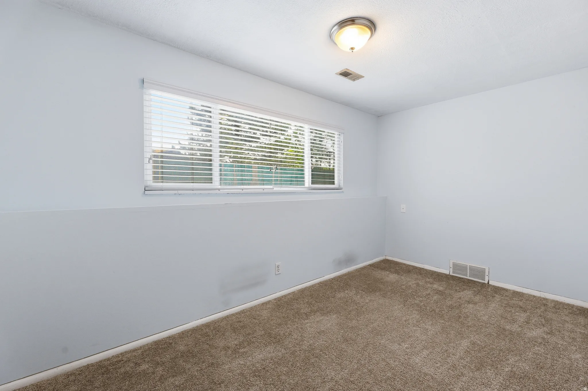 Carpeted room featuring a single window with horizontal blinds, a ceiling-mounted light fixture, and an air vent