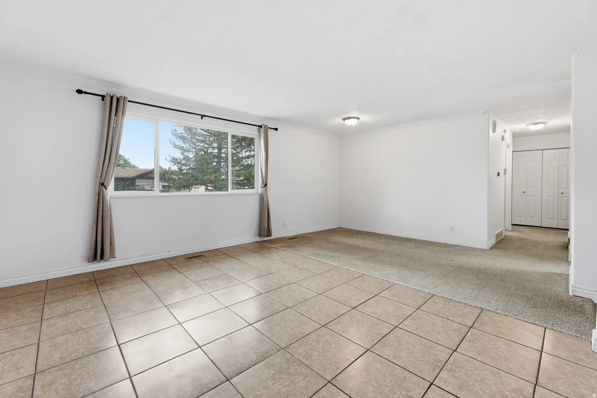 Spacious room featuring a large window, tile flooring, and carpeted areas