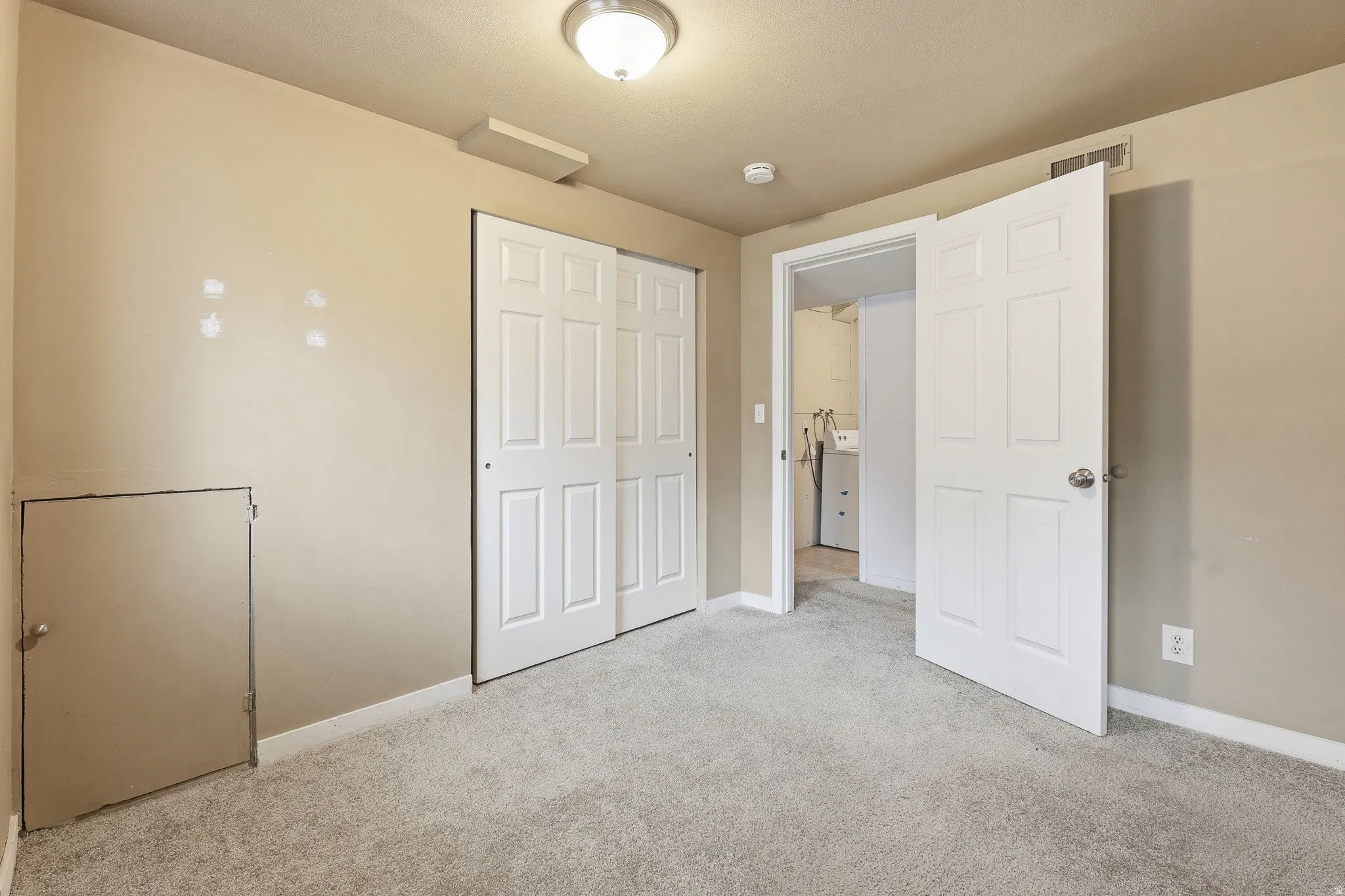 Carpeted room with neutral wall tones, featuring a six-panel bi-fold closet, a six-panel door leading to an additional space, and a flush mount ceiling light fixture