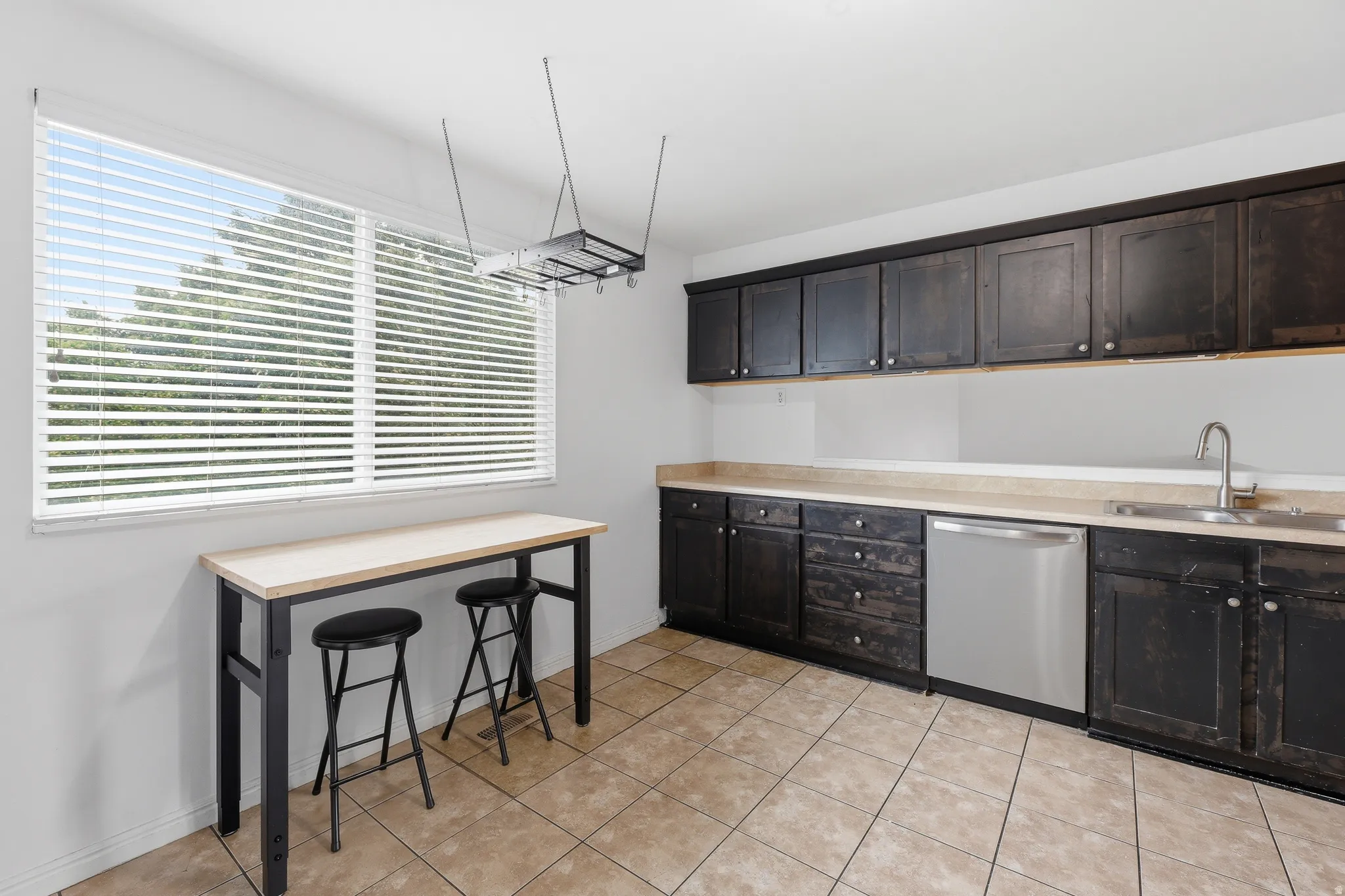 Kitchen featuring dark cabinetry, a stainless steel dishwasher, a single basin sink with a chrome faucet, light-toned countertops, and tiled flooring