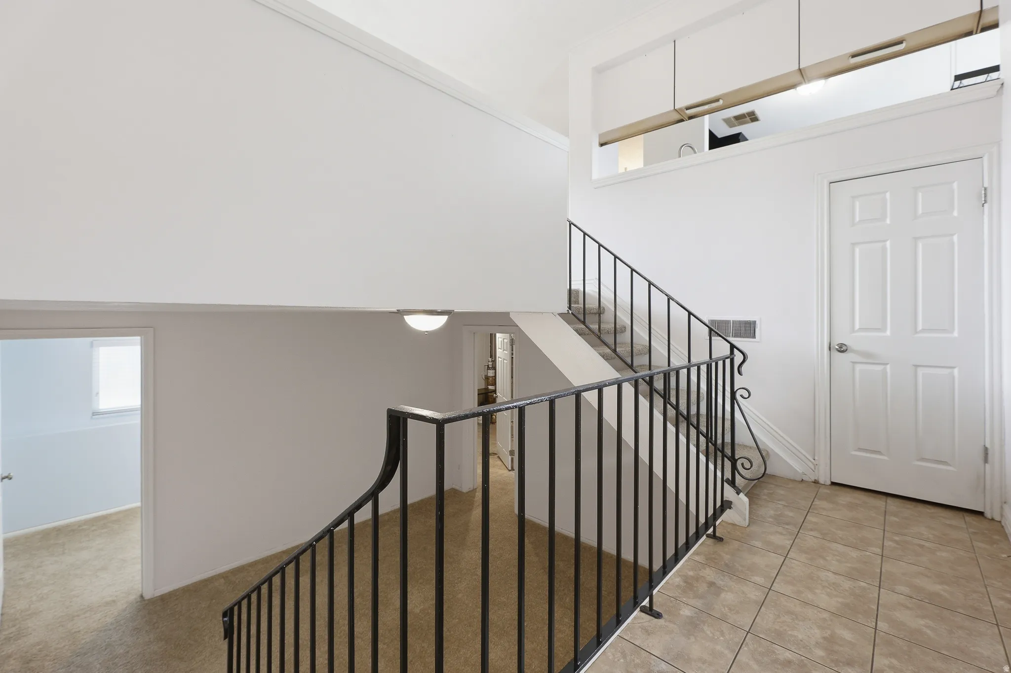 Interior staircase with wrought iron railing and light-colored carpeted treads