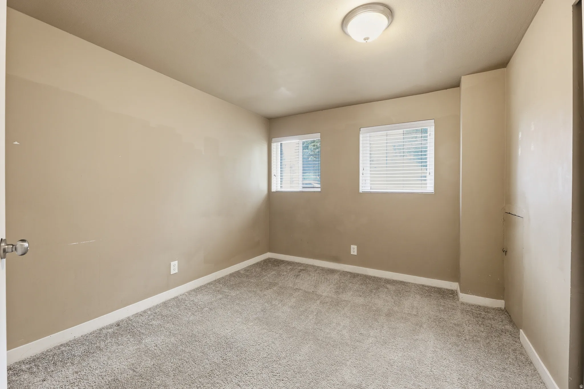 Neutral tone walls with white trim, two windows featuring white blinds, and gray textured carpeting