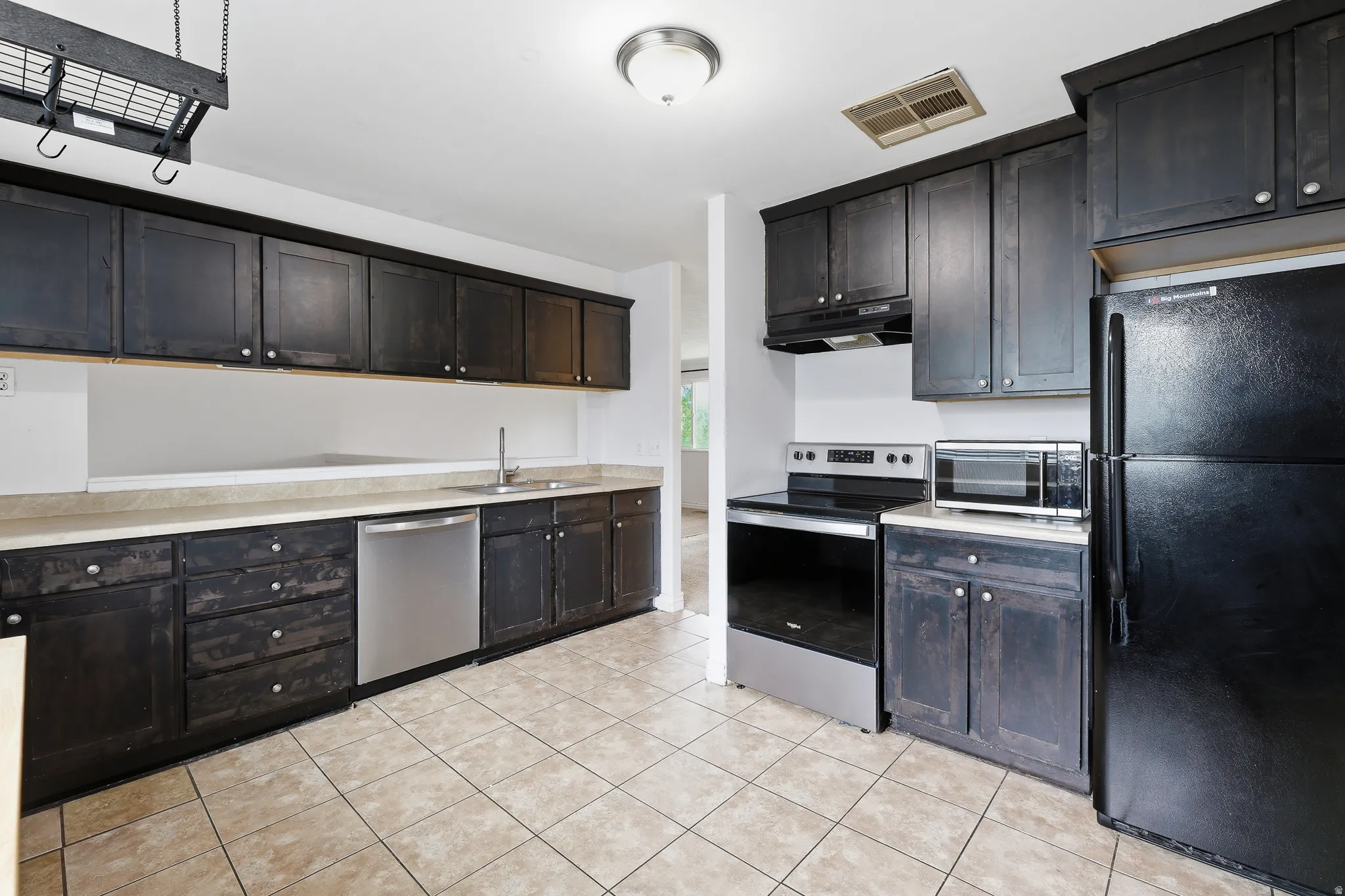Kitchen featuring dark wood cabinetry, a stainless steel dishwasher, and neutral-toned tile flooring