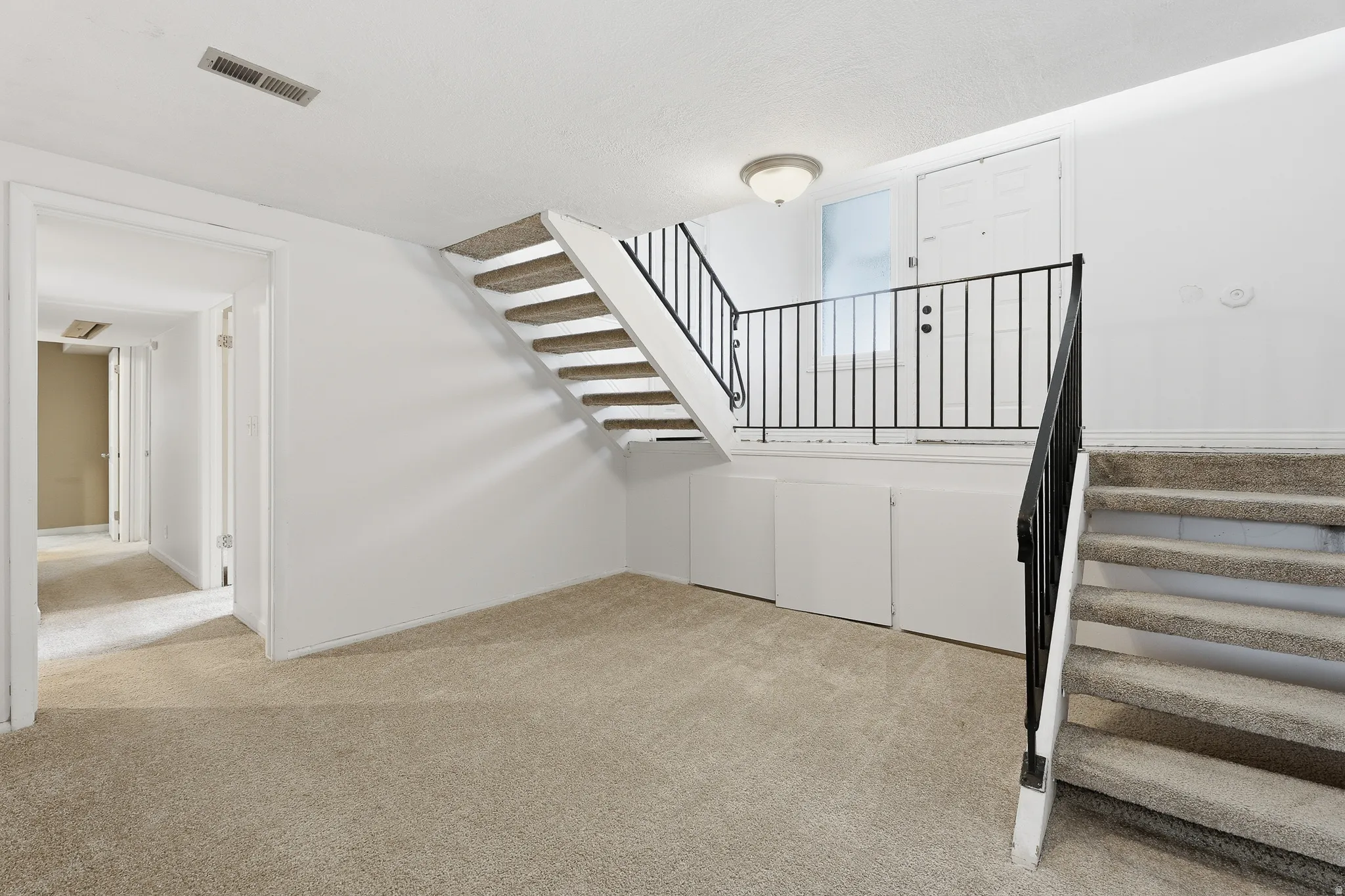 Carpeted flooring throughout, featuring a staircase with black metal railings and a built-in storage area