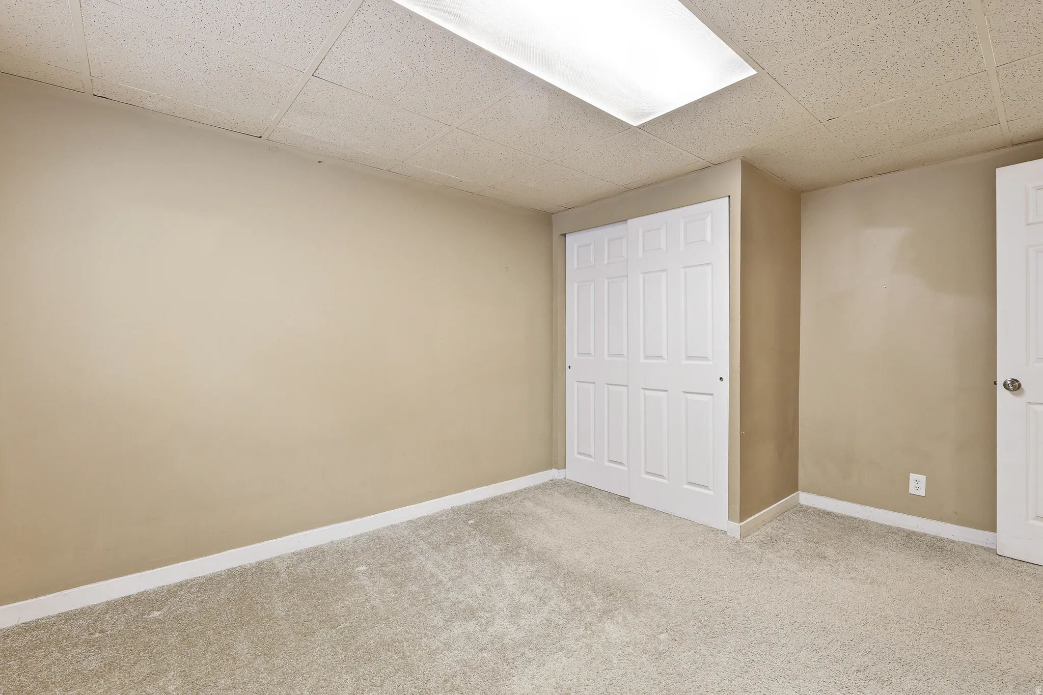 Neutral-toned room featuring light-colored carpeting and a drop ceiling with integrated rectangular lighting