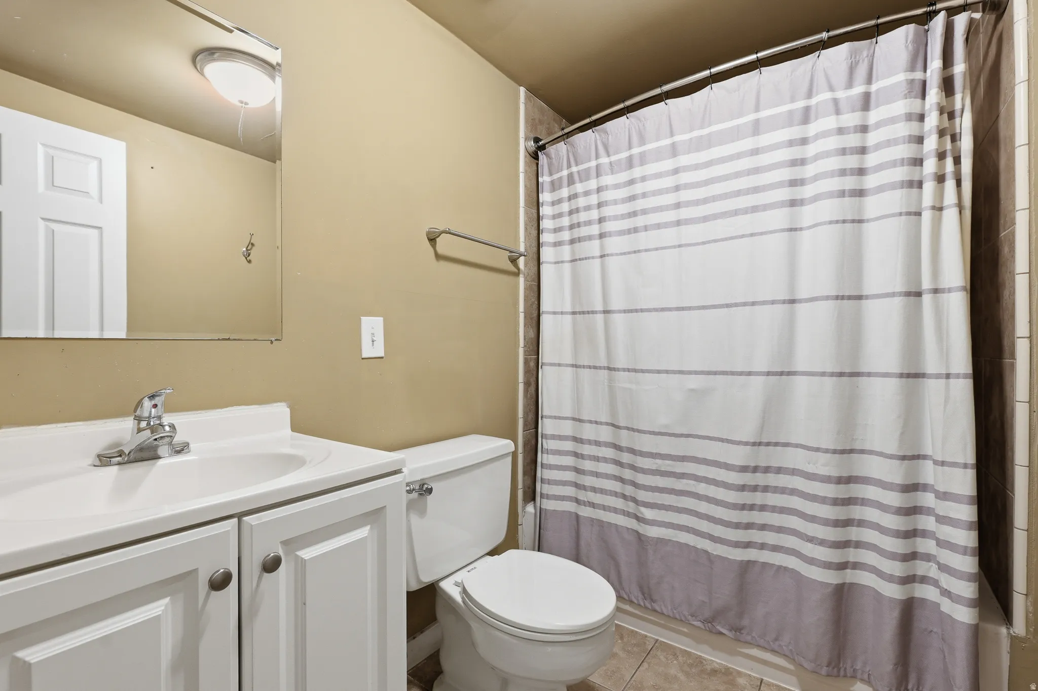 Bathroom featuring a white vanity with integrated sink, chrome faucet, wall-mounted mirror, toilet, and tiled shower surround
