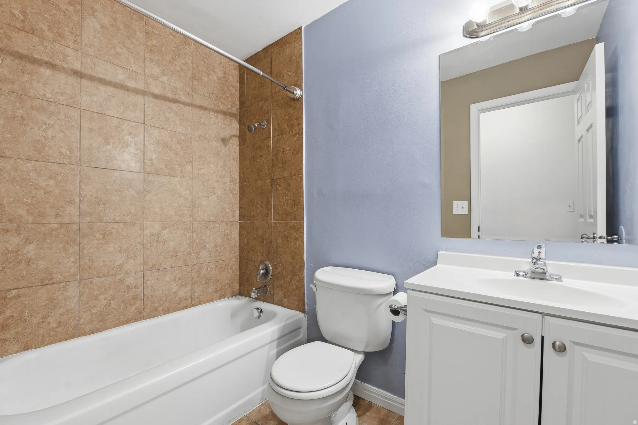 Bathroom featuring a porcelain tub, floor-to-ceiling tile surround, white vanity with integrated sink, and silver-finish fixtures