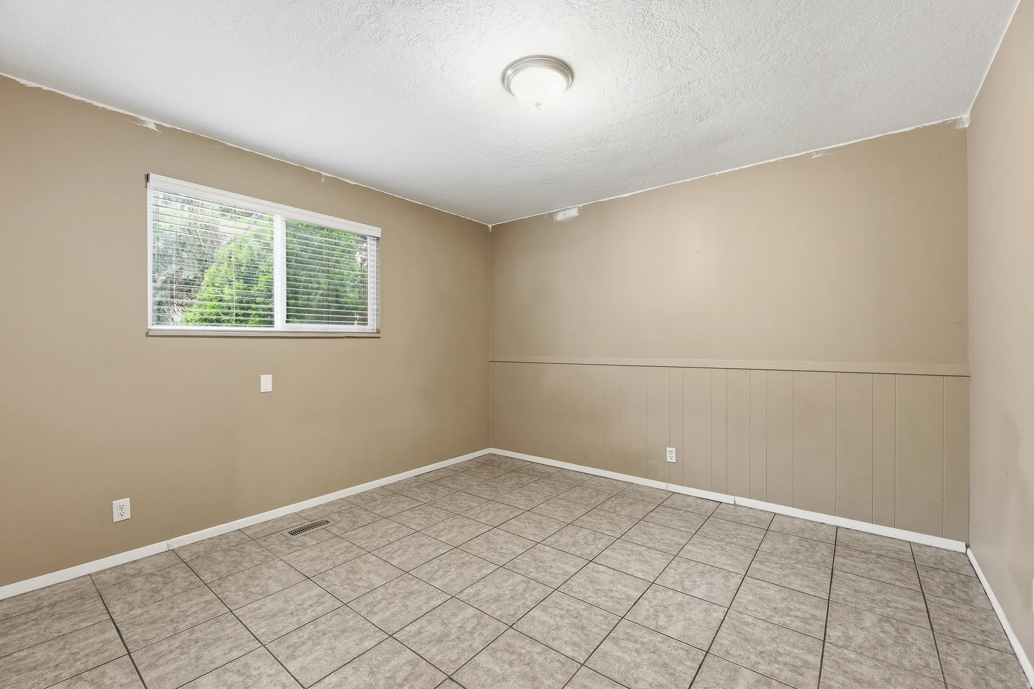 Room featuring neutral tone walls, tile flooring, a window with horizontal blinds, wainscoting, and a ceiling-mounted light fixture