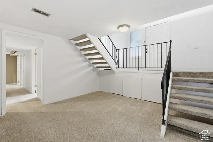 Carpeted flooring throughout, featuring a staircase with black metal railings and a built-in storage area