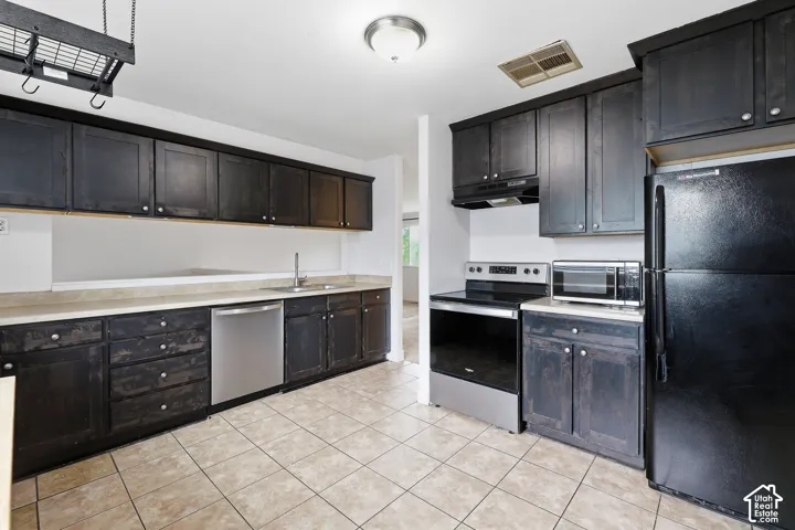 Kitchen featuring dark wood cabinetry, a stainless steel dishwasher, and neutral-toned tile flooring