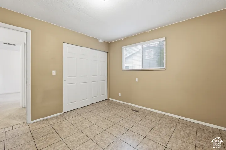 Spacious room featuring tile flooring, a window with blinds, and a closet with bifold doors