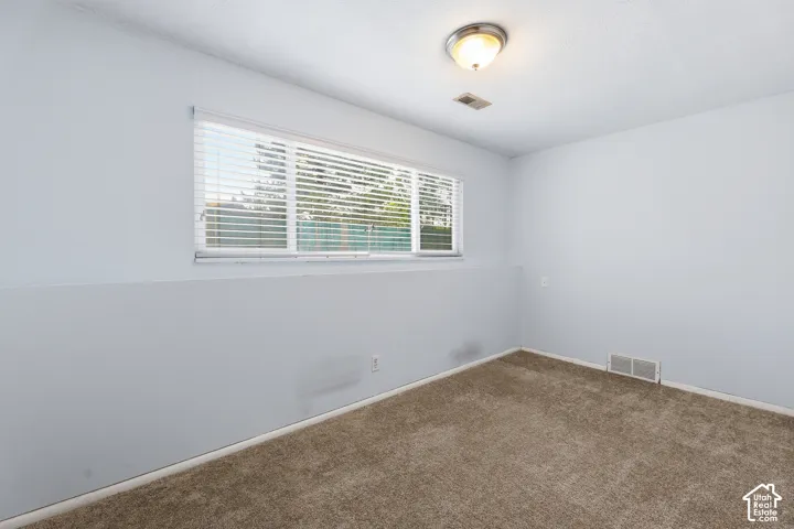 Carpeted room featuring a single window with horizontal blinds, a ceiling-mounted light fixture, and an air vent