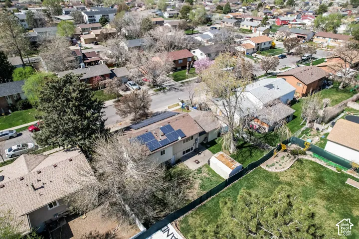 Aerial perspective showcasing a residential property with solar panels, a brown shingle roof, and a mature tree in the front yard