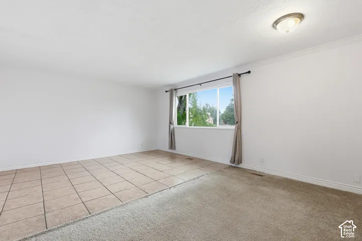 Spacious room featuring a large window, mixed flooring with ceramic tile and carpet, crown molding, and an overhead flush-mount light fixture