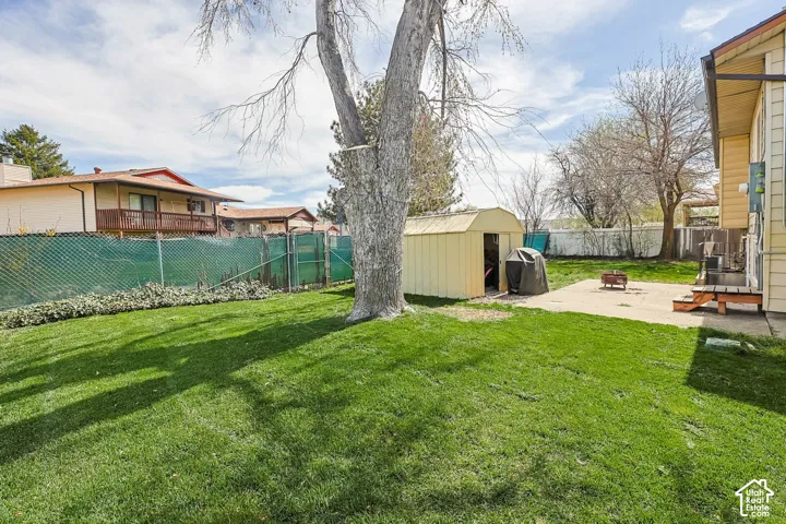 Expansive rear yard featuring a large grass area, mature trees, a concrete patio, and a storage shed
