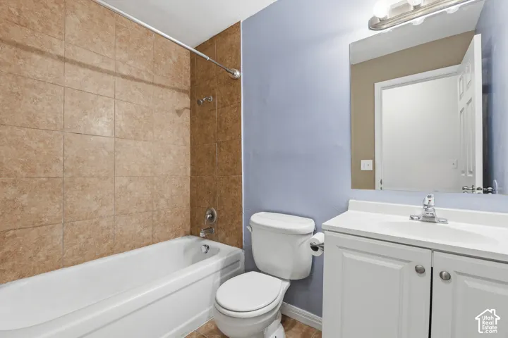 Bathroom featuring a porcelain tub, floor-to-ceiling tile surround, white vanity with integrated sink, and silver-finish fixtures