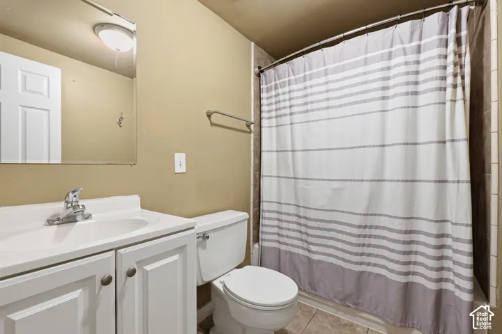 Bathroom featuring a white vanity with integrated sink, chrome faucet, wall-mounted mirror, toilet, and tiled shower surround
