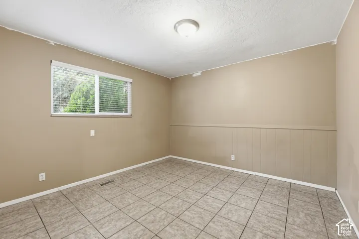 Room featuring neutral tone walls, tile flooring, a window with horizontal blinds, wainscoting, and a ceiling-mounted light fixture
