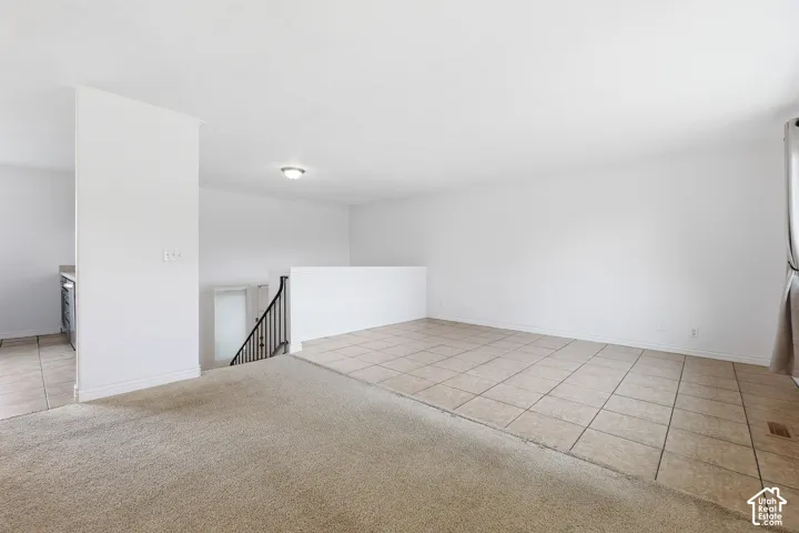 Spacious room featuring a combination of light-colored carpeting and large square floor tiles