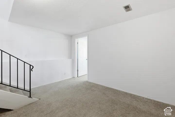 Carpeted room featuring a staircase with black metal railing, white painted walls, and a white paneled door