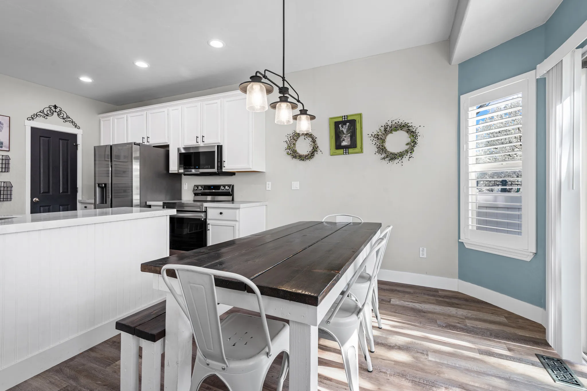 Kitchen featuring stainless steel appliances, white cabinetry, dark wood-style flooring, and hanging light fixtures