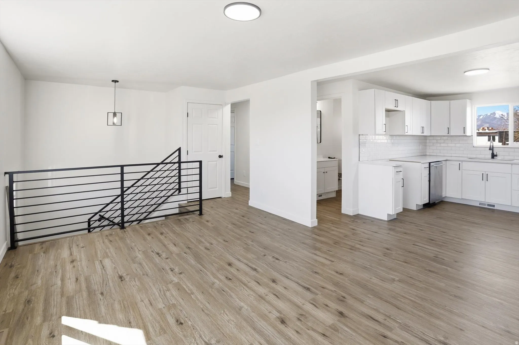 Kitchen with light countertops, white cabinetry, light wood-type flooring, and hanging light fixtures