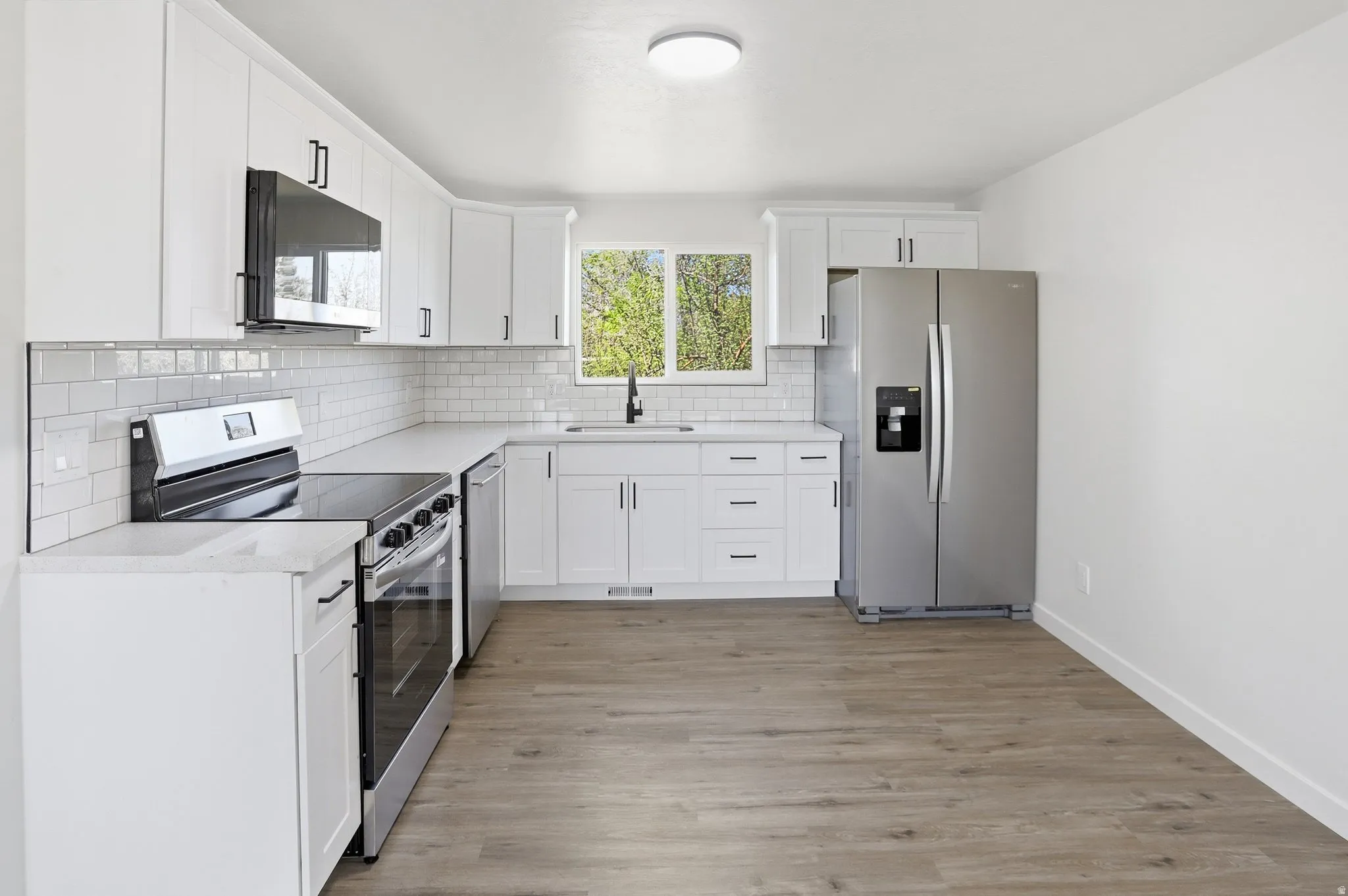 Kitchen with stainless steel appliances, white cabinetry, light wood-style flooring, tasteful backsplash, and light stone countertops